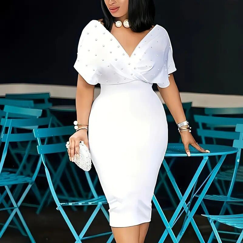 Woman in a white dress with pearl embellishments standing in front of blue chairs.