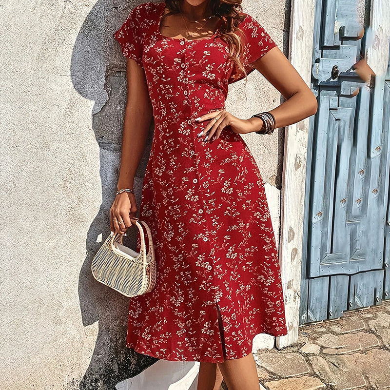 Woman in a red floral dress standing against a textured wall with a blue door.
