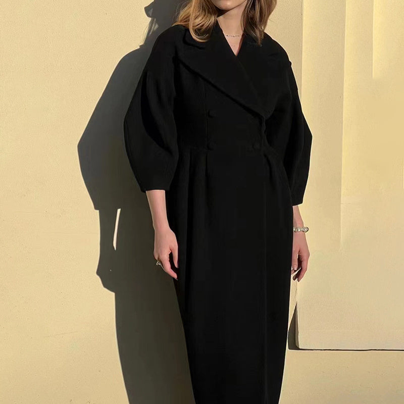 Person wearing a black coat against a beige wall