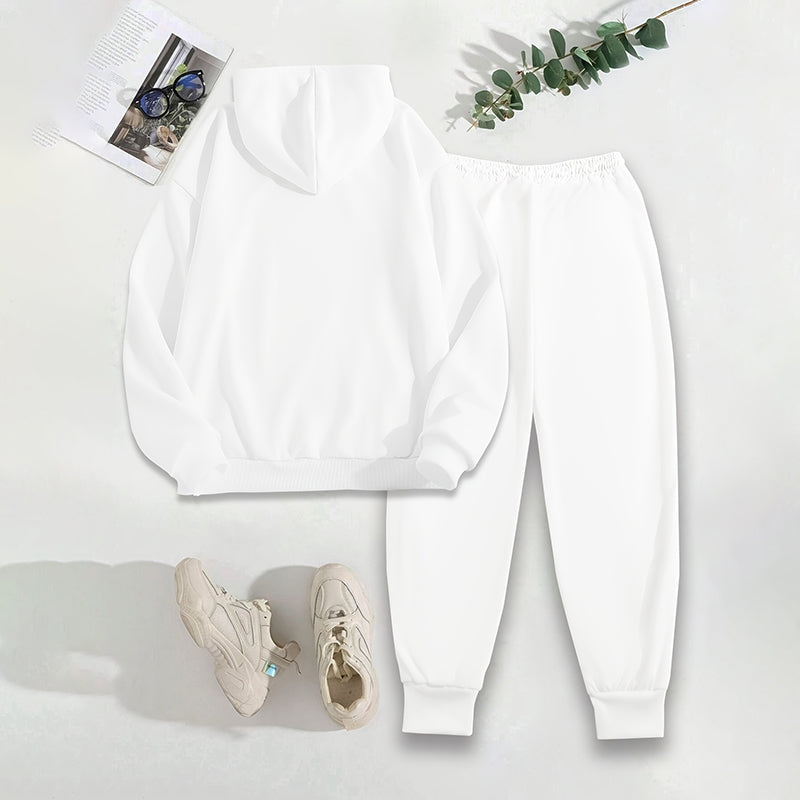 White sweatshirt, pants, and sneakers on a white surface with a plant and magazine.