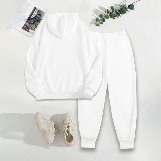 White sweatshirt, pants, and sneakers on a white surface with a plant and magazine.