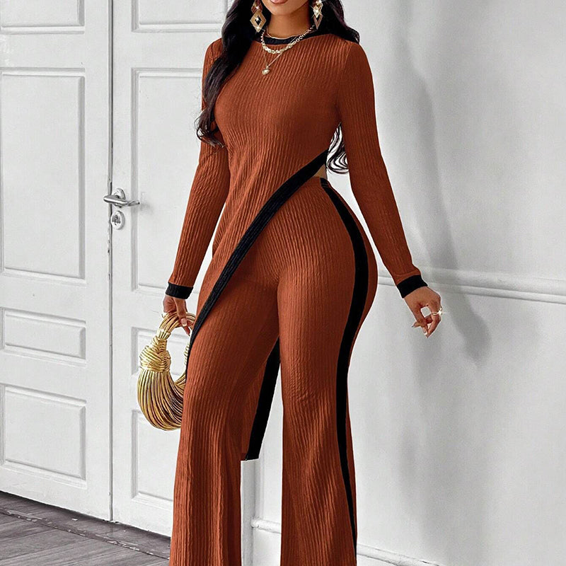 Woman wearing a brown ribbed jumpsuit with black accents, standing against a white wall.