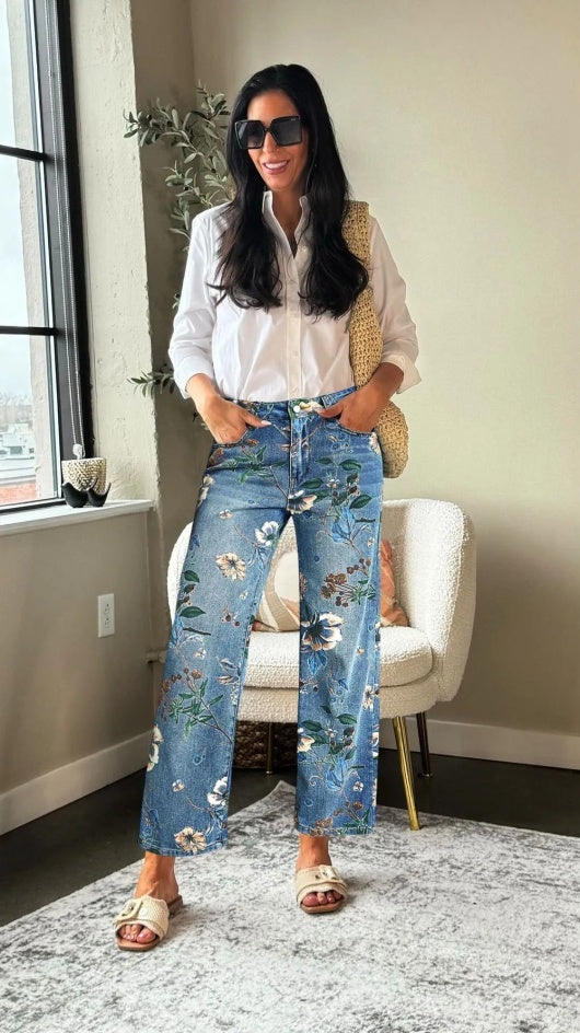 Woman wearing a white blouse and floral jeans in a room with a window and chair.