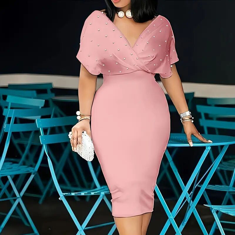 Woman in a pink dress with pearl embellishments standing among blue chairs.