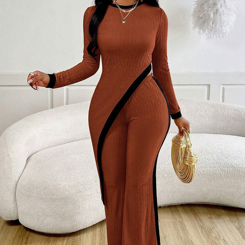 Woman wearing a brown ribbed jumpsuit with black side panels, holding a gold clutch in a living room.