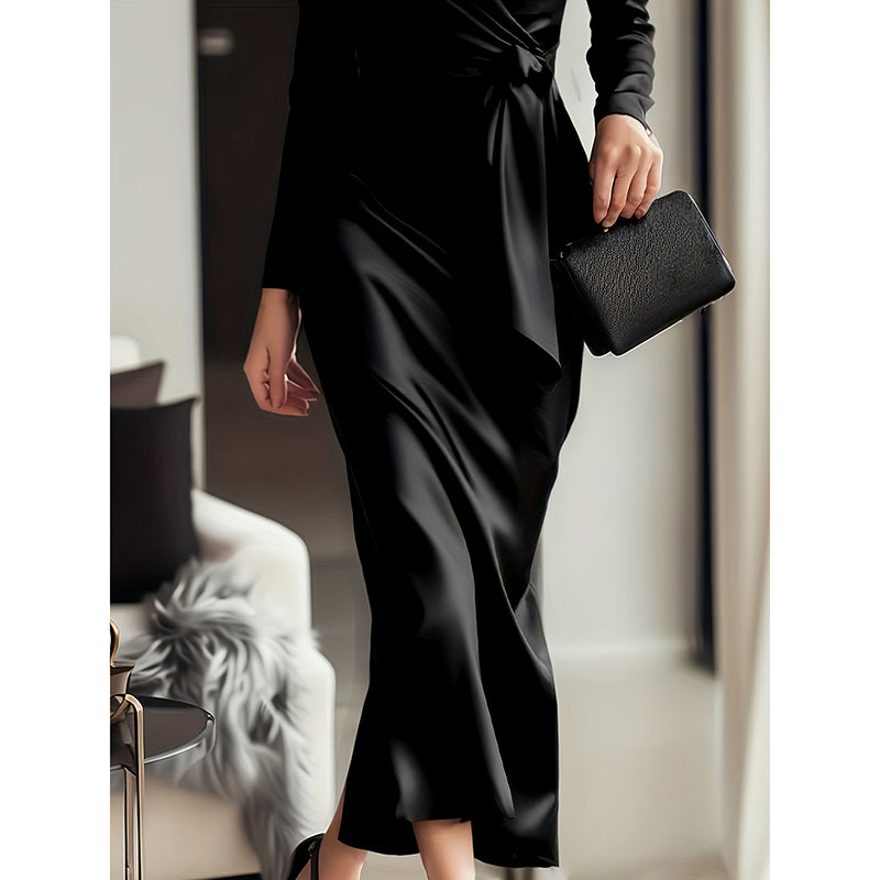 Person wearing a black satin dress holding a matching clutch in an indoor setting.